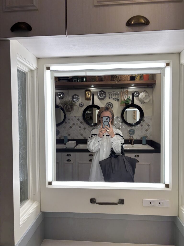 白いロングワンピースを着た女性が鏡越しに自撮りしている写真。室内はアンティーク風のインテリア。