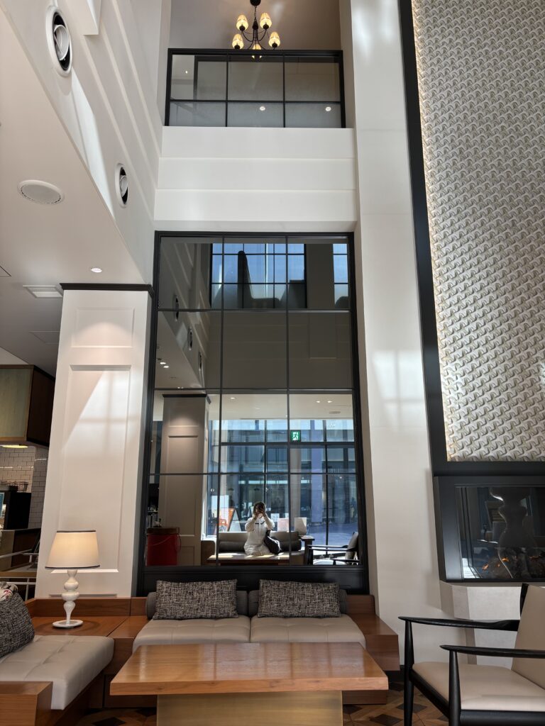 カフェラウンジの大きな鏡越しに、ソファとテーブル、そして撮影者が座っている様子が写っている写真。